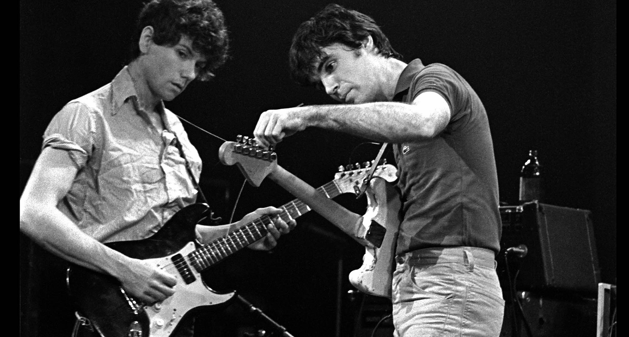Talking Heads live at CBGB&#039;s, in 1977. On the right, David Byrne tuneshis Fender Strat, while Jerry Harrison – also playing a Strat – looks on.