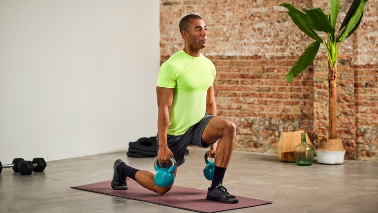 Man uses kettlebells as he performs a lunge during a workout