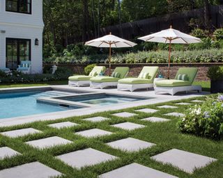 Pale green and white sun loungers beside a swimming pool and square paving stones laid into a lawn.