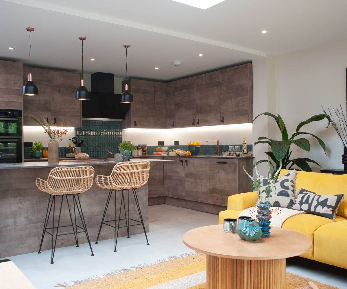 A kitchen-diner with a yellow sofa and wooden panelled kitchen cabinets with overhead lights