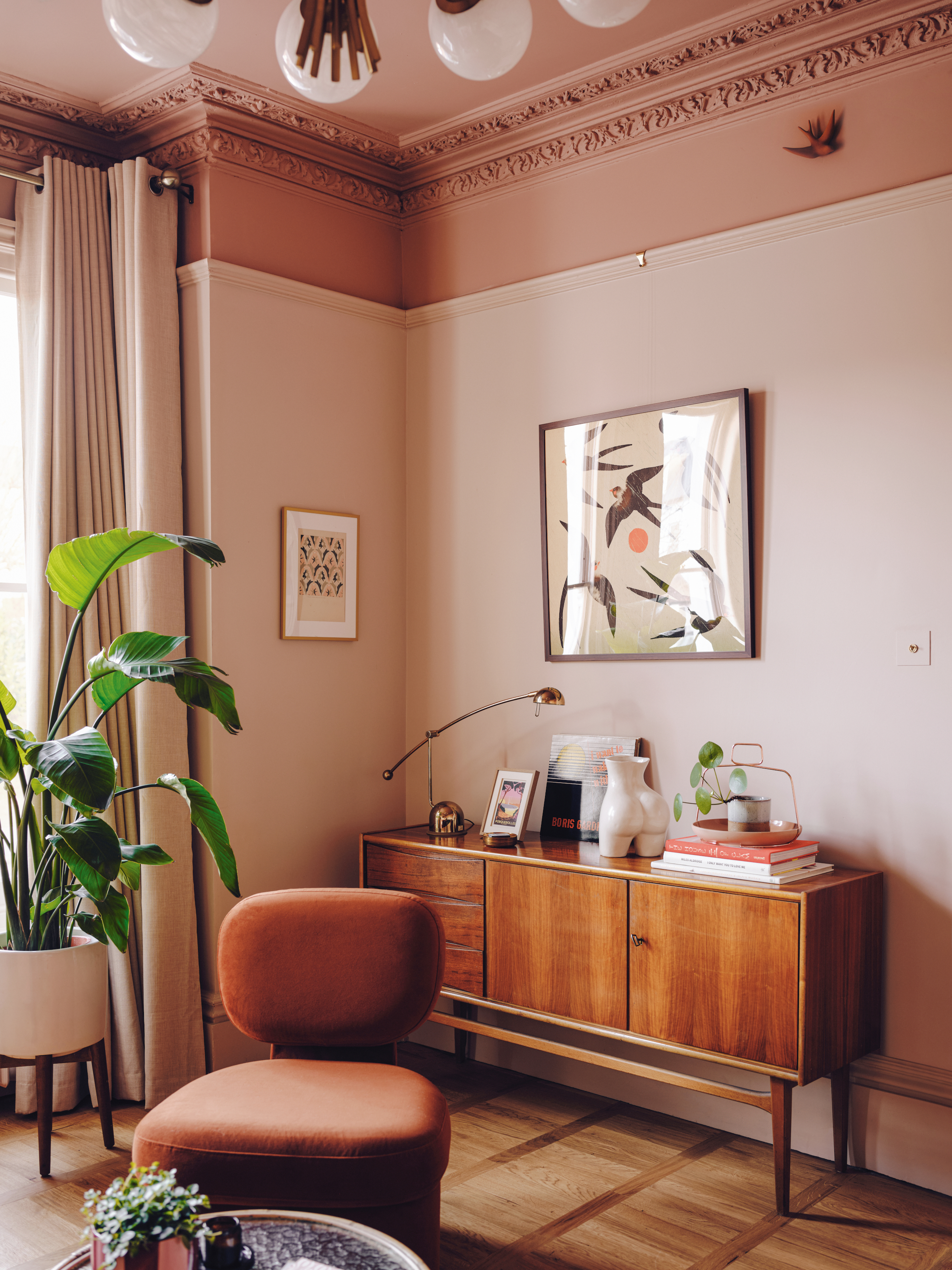 Corner of a pink living room with mid-century sideboard and rust orange accent chair