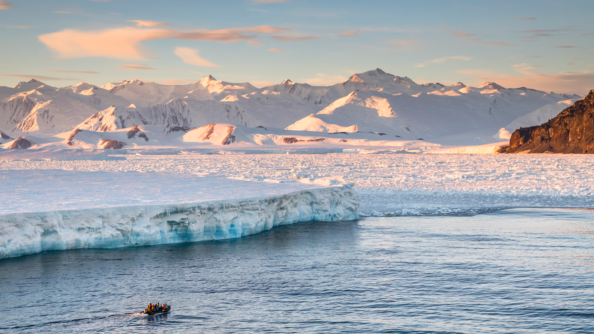 A small raft full of people is next to a large icy glacier