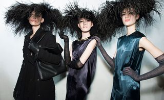 Three models wearing dark clothes featuring feathers and a headpiece