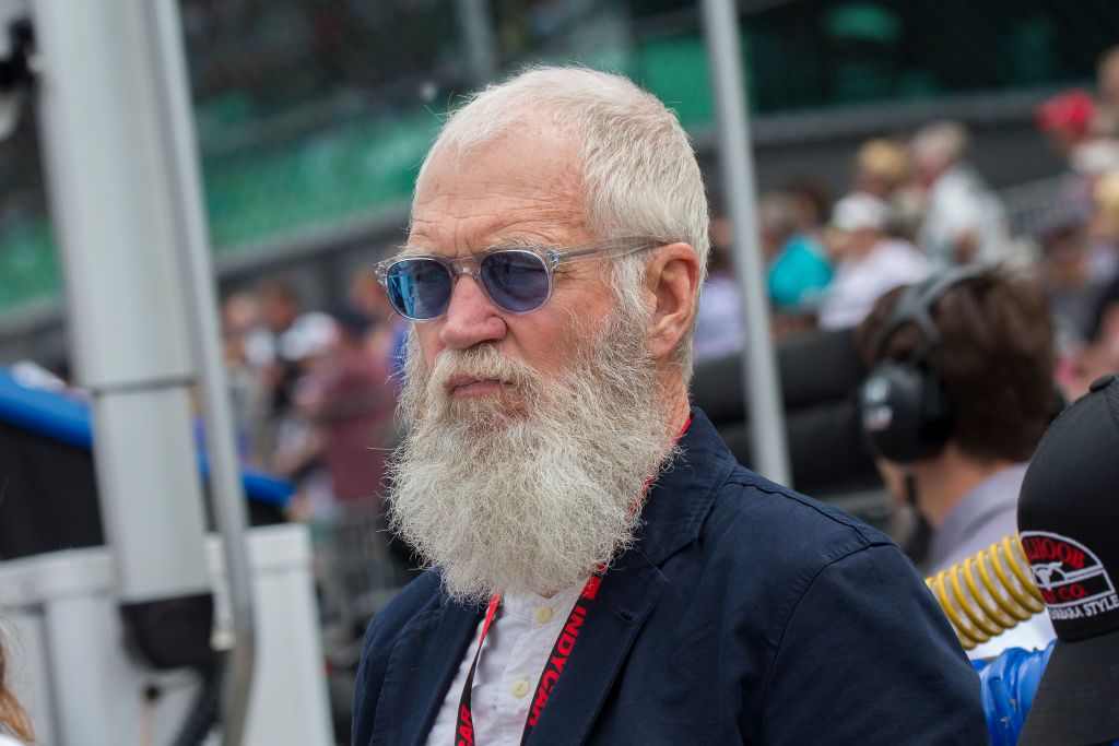 David Letterman with a bushy beard wears blue sunglasses and an orange lanyard.