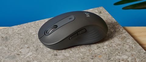 a black mouse with a scroll wheel, two side buttons, and grooved edges, with a logi logo, sits atop a pale table with a blue background