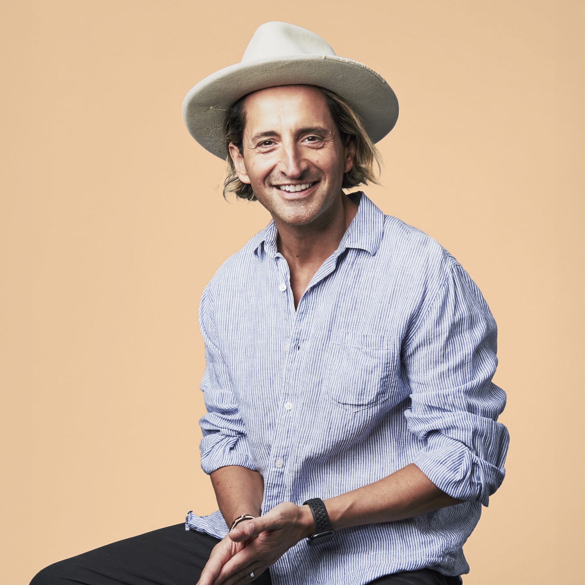 a professional photo of a man with short, blonde hair wearing a blue button up shirt and a cream hat
