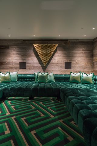 green movie room with button backed sectional and patterned rug, wood walls, green cushions