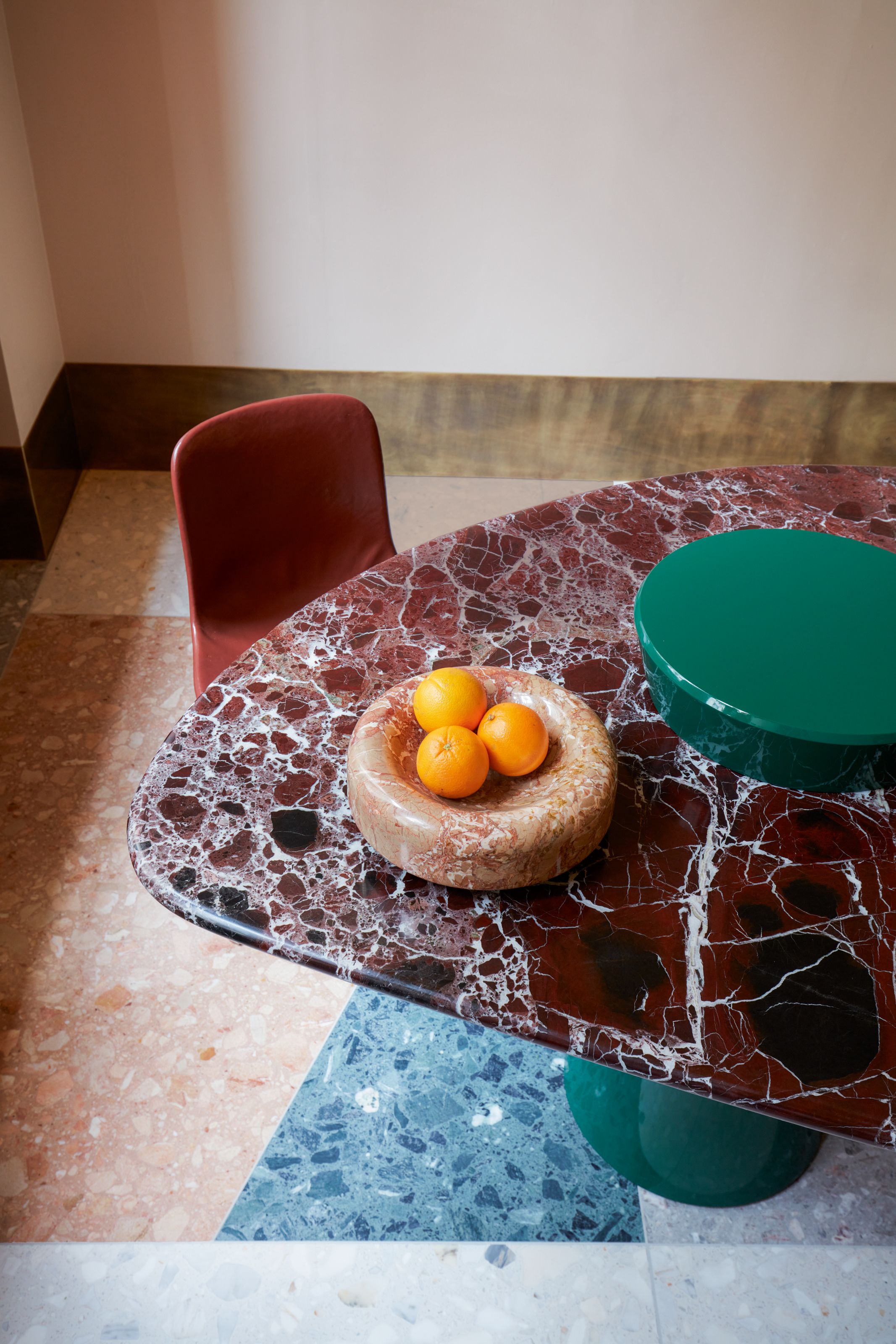 Burgundy marble table with glossy green base on a multicoloured terrazzo floor