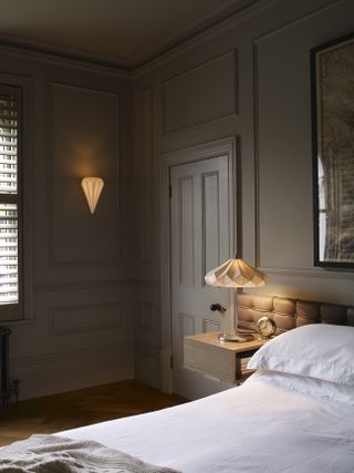 Bedroom with dark neutrals walls and wall light and table lamp on night stand