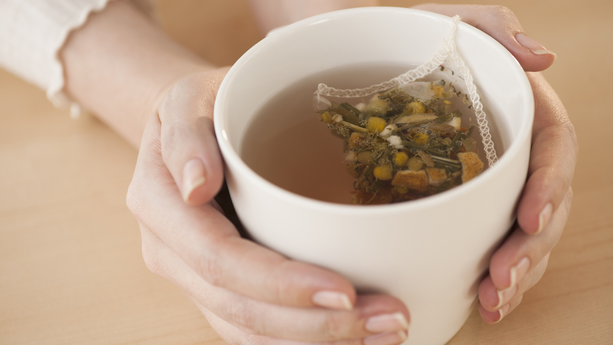 A person holds a white mug filled with chamomile tea