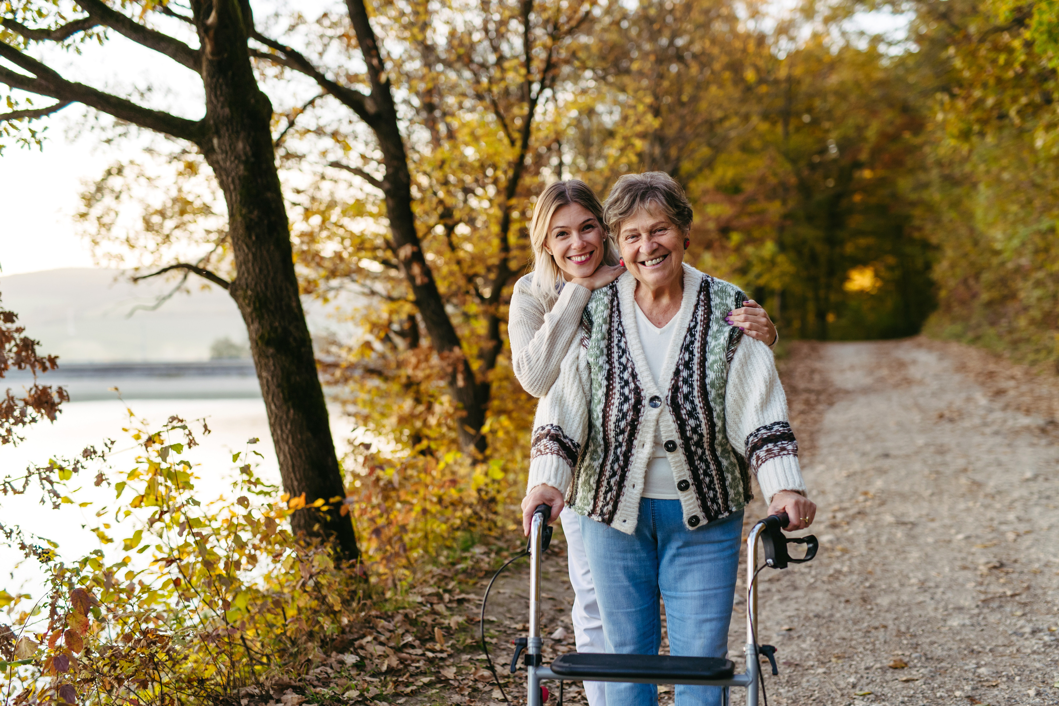 Nurse and female senior patient with a walker on a stroll in autumn nature. Managing chronic illness expenses in retirement.