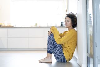 Serious woman sitting on floor leaning against a wall at home