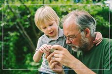 A grandfather and a young boy looking at something together in the garden