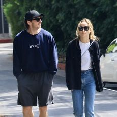 Olivia Wilde wearing a navy shirt, white t-shirt, blue jeans, and yellow sneakers