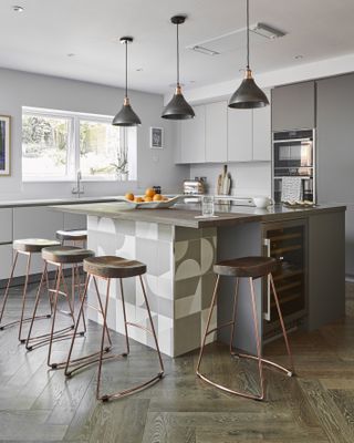 a grey kitchen with large island with breakfast bar, storage and statement lighting
