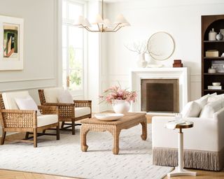 white living room with beige sofa and rug, woven set of armchairs, wicker coffee table with vase of pink flowers and brass pendant light