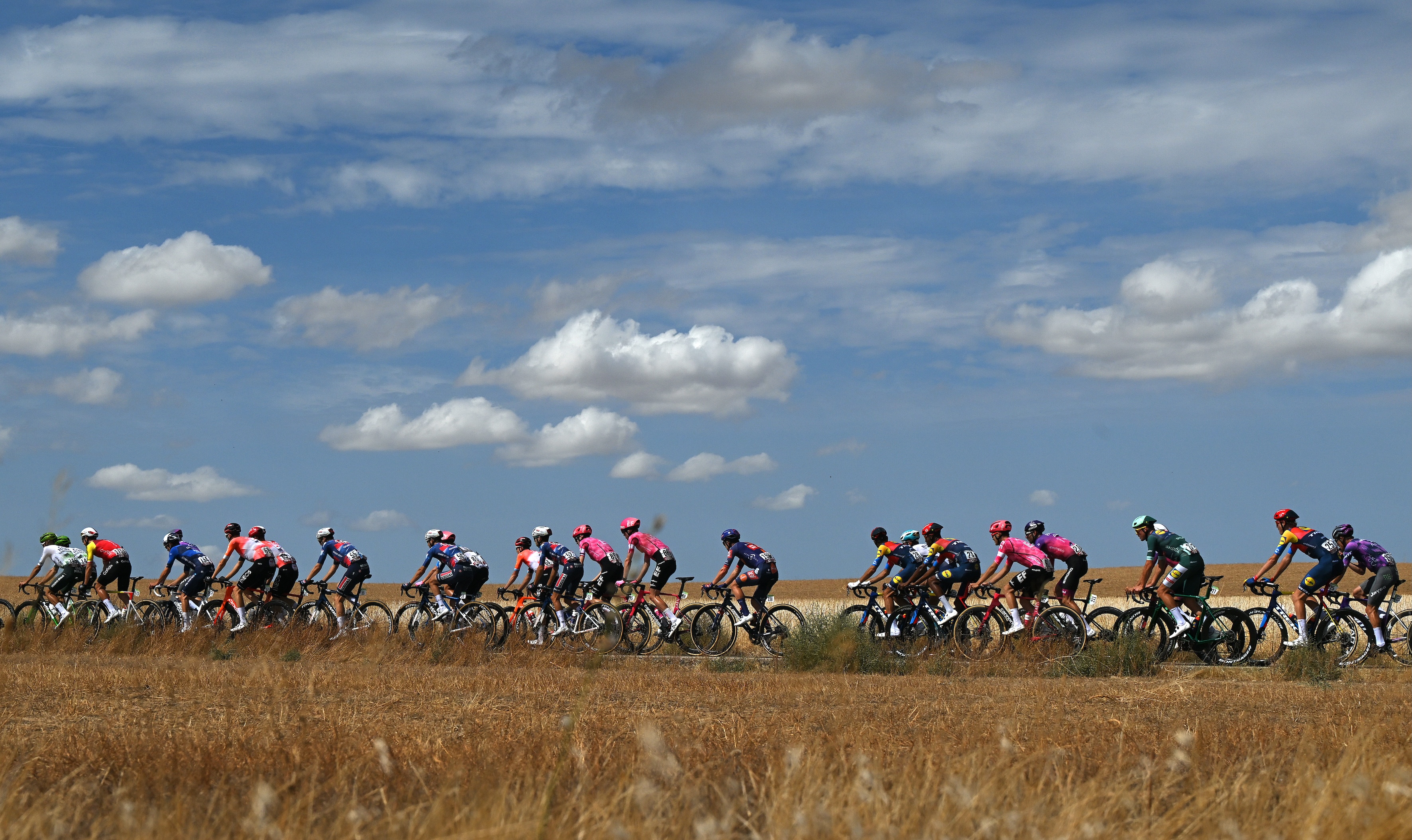 Vuelta a Espana 2025 peloton rides through fields under scudding clouds