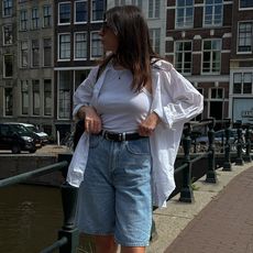 Woman on street wears white shirt, tank top and long denim shorts