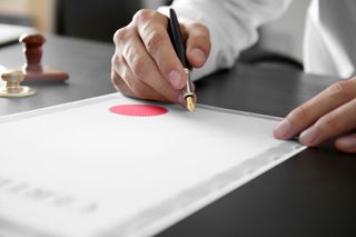 A close-up shot of a businessperson writing on a certificate with a fountain pen.