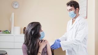 Woman with surgical mask receiving vaccine from doctor