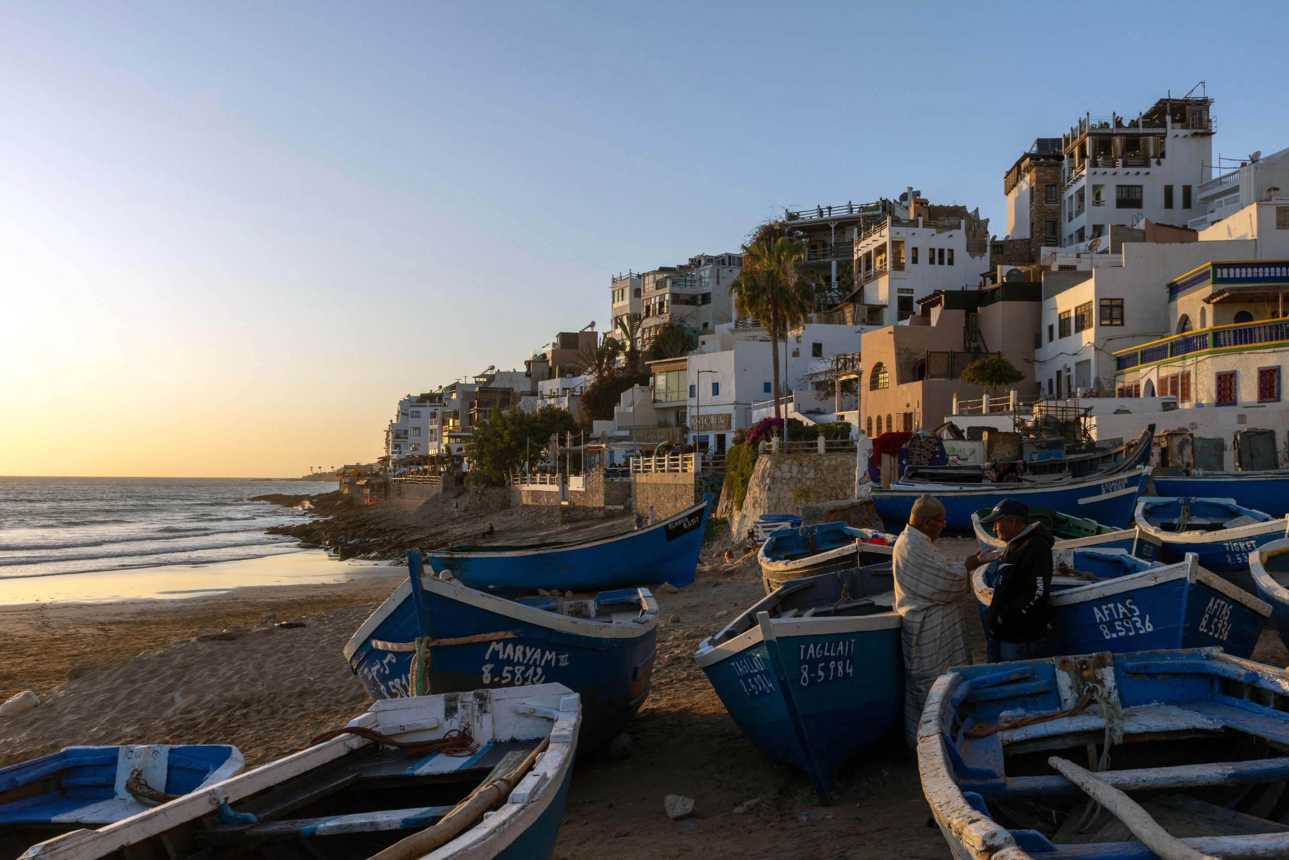 A view of the beach and some houses in taghazout, with blue fishing boats stacked high