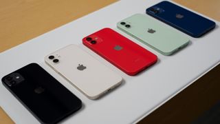 Five iPhone 12 models in black, white, red, green, and blue displayed on a table