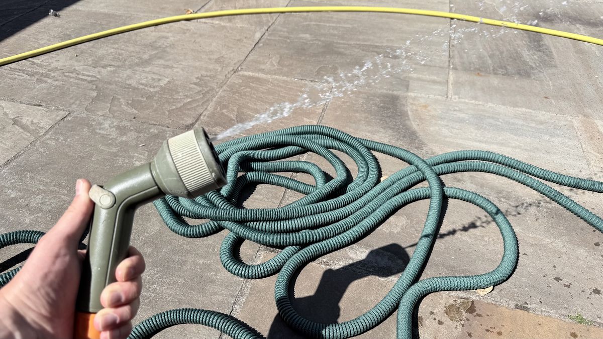 The Pocket Hose on the floor with a hose head in hand spraying water