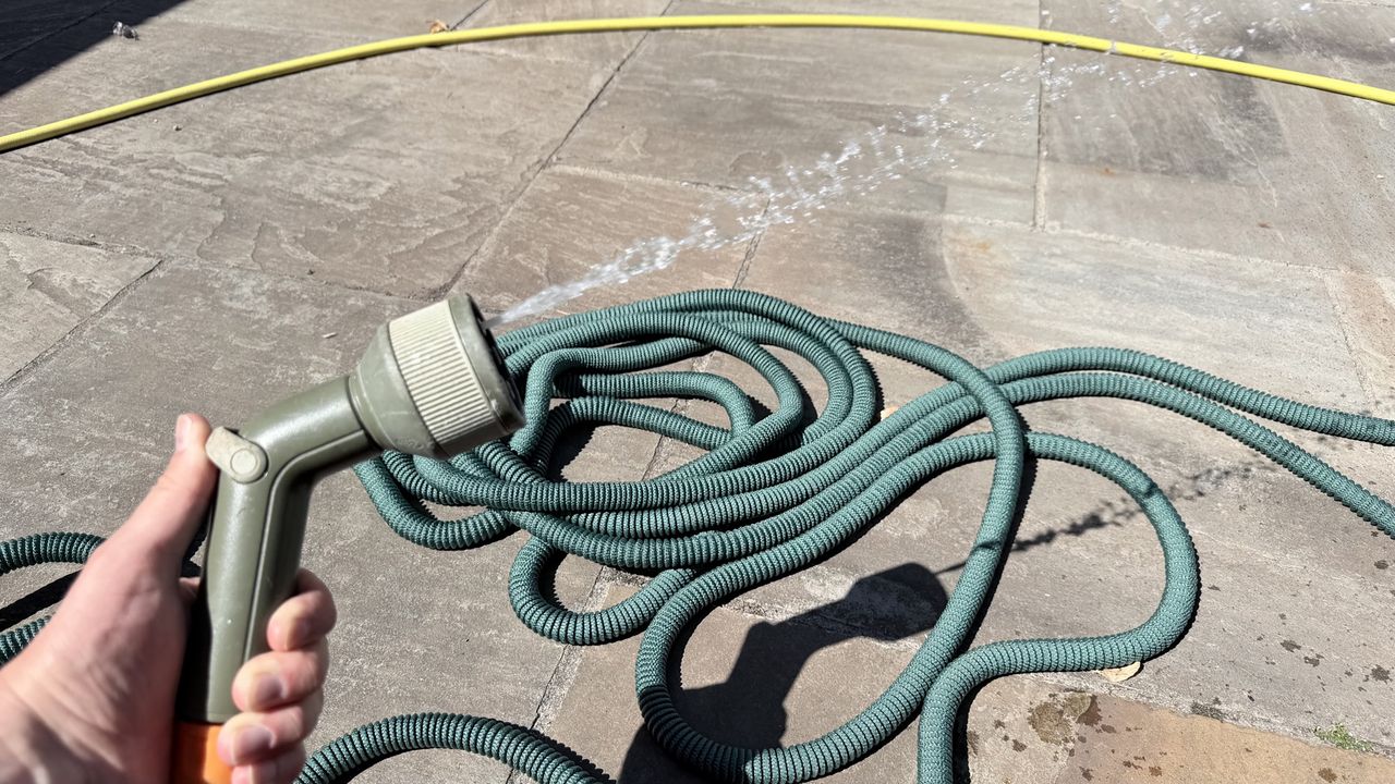 The Pocket Hose on the floor with a hose head in hand spraying water