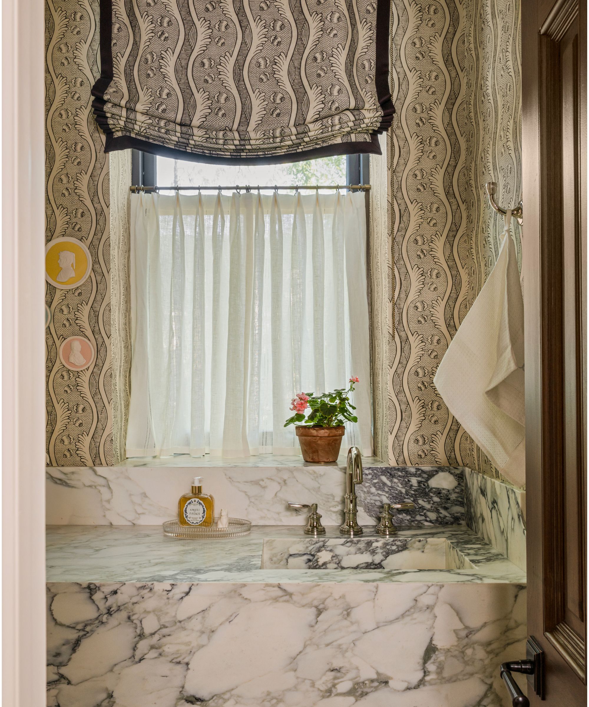 a pattern drenched powder room with matching wallpaper and window blind with a large marble vanity