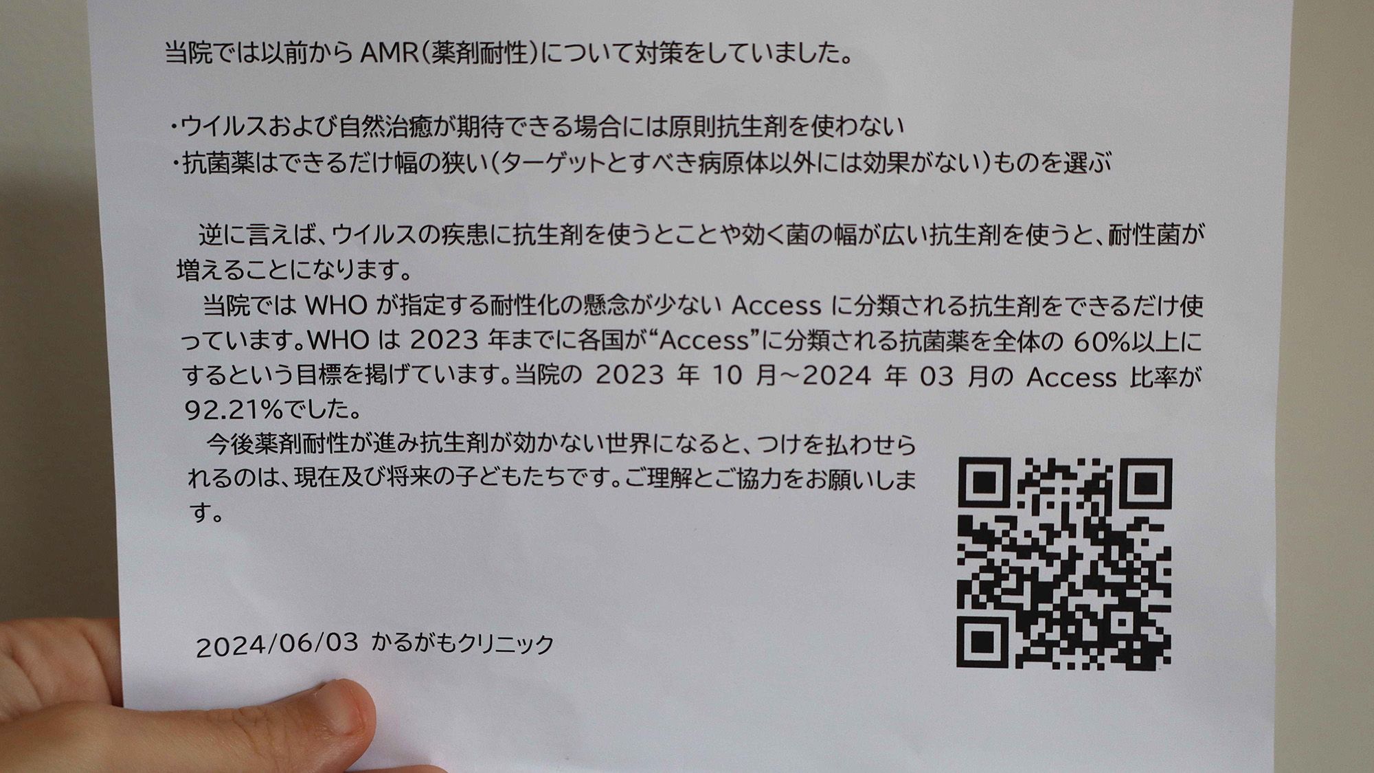 A person holds a piece of paper with Japanese writing on it and a QR code