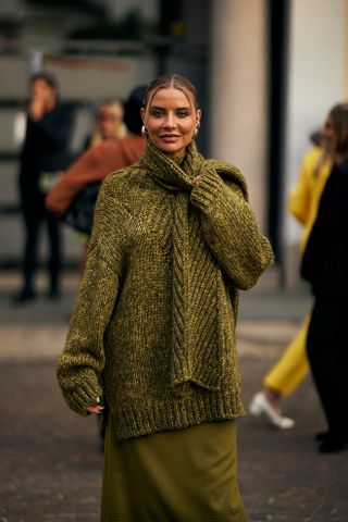 A blond fashion week guest wearing the English country style trend of a green turtleneck sweater and green skirt.