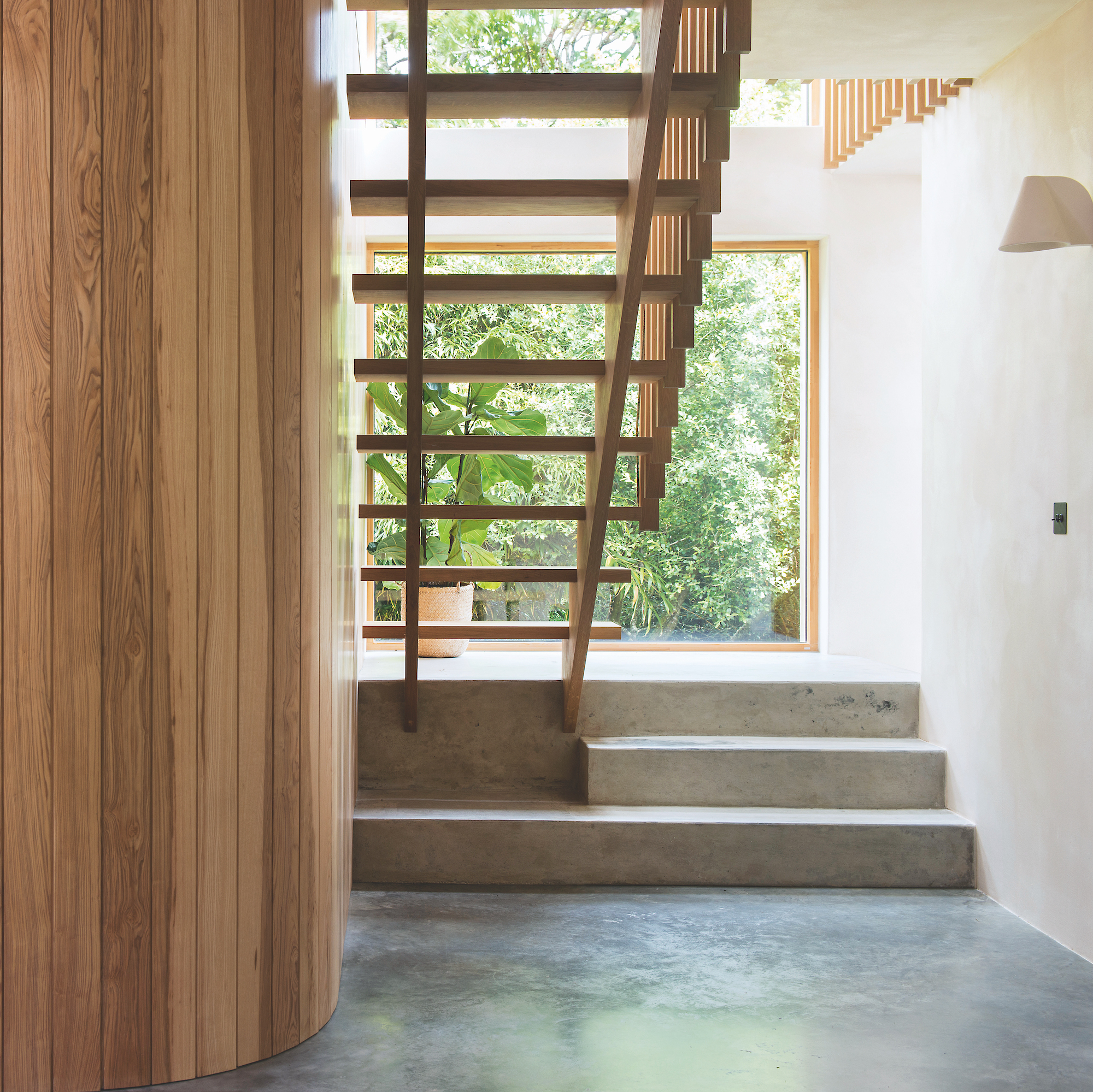hallway and staircase of contemporary house with micro-cement floor, open-tread wooden staircase and curved wooden wall