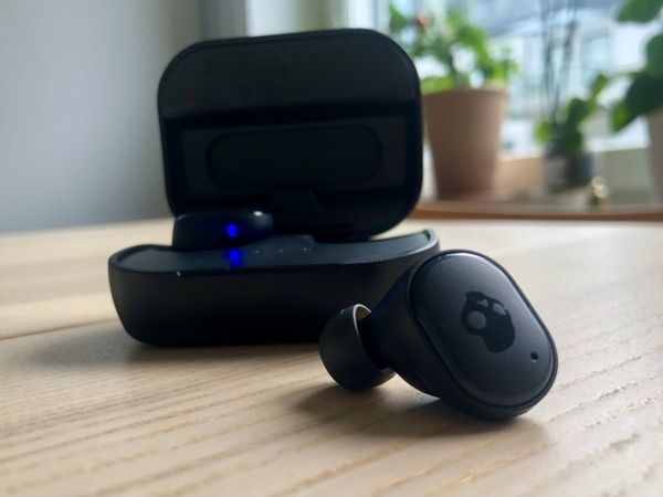 En Skullcandy Grind True Wireless Earbuds-hörlur som ligger på ett bord framför sitt laddningsfodral.