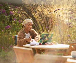 Woman working at laptop at idyllic garden cafe table