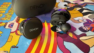 Denon PerL Pro earbuds on a colorful psychedelic background.
