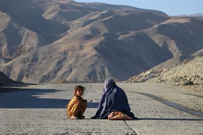 An Afghan burqa-clad woman sits beside a girl, as they look for alms along a street in the Fayzabad district of Badakhshan province 