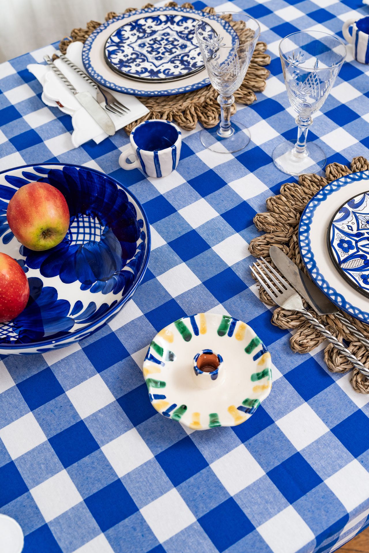 Image from above of a table with a blue and white check tablecloth, rattan placemats, and blue and with ceramic tableware.