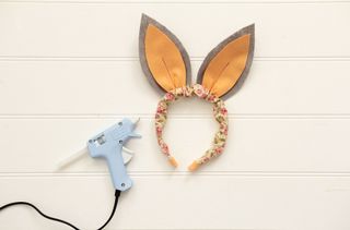A glue gun next to a pair of bunny ears on a table.