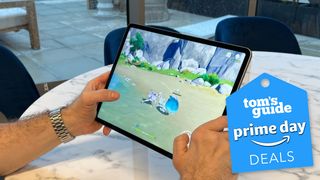 An iPad Pro 2022 being held while playing a video game with a white table and blue seats in the background.