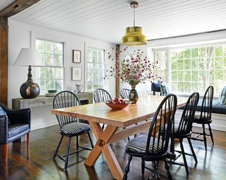 dining room with white shiplap boardine, wooden trestle table, black Windsor chairs and brass pendant