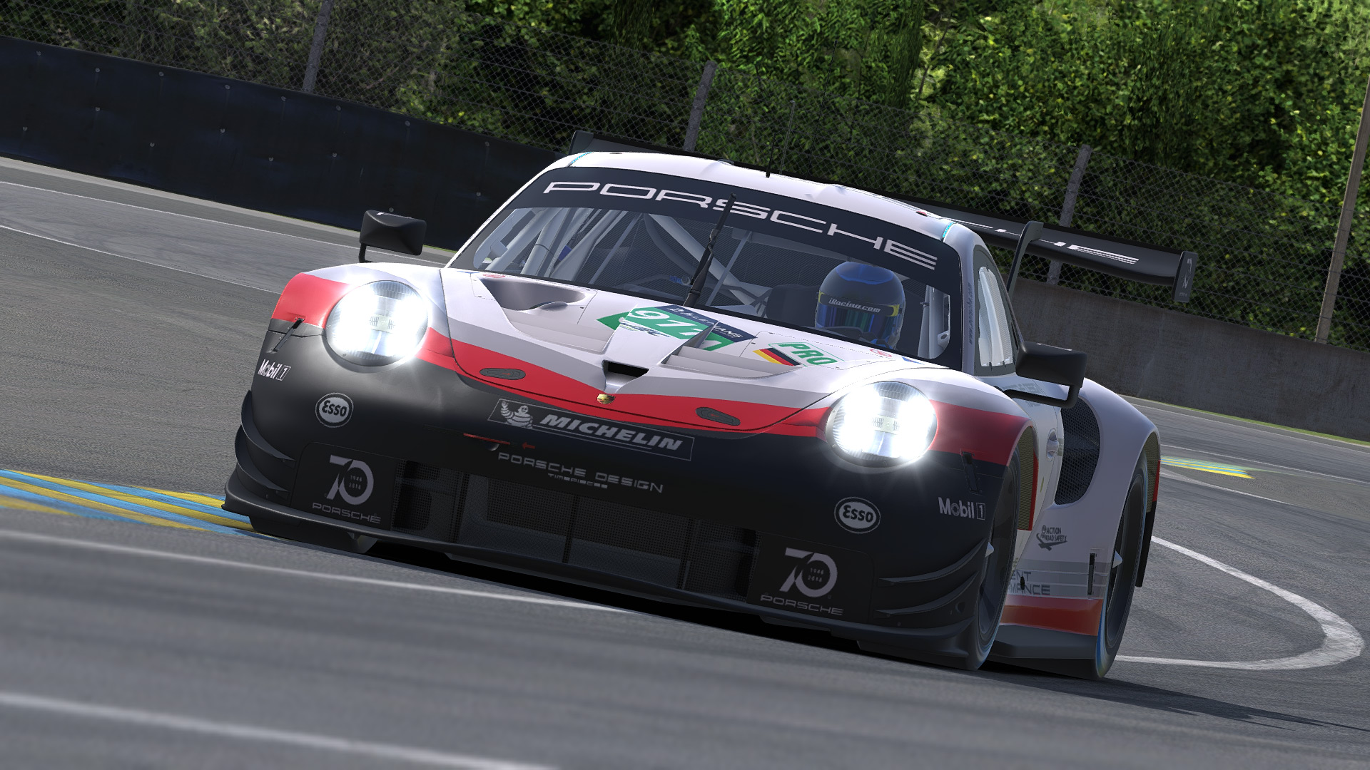A silver, red and black Porsche races down a track with trees in the background
