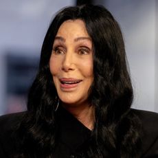 A headshot of Cher wearing a black jacket and looking to the left