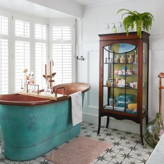 Glass cabinet in a white bathroom with copper bath