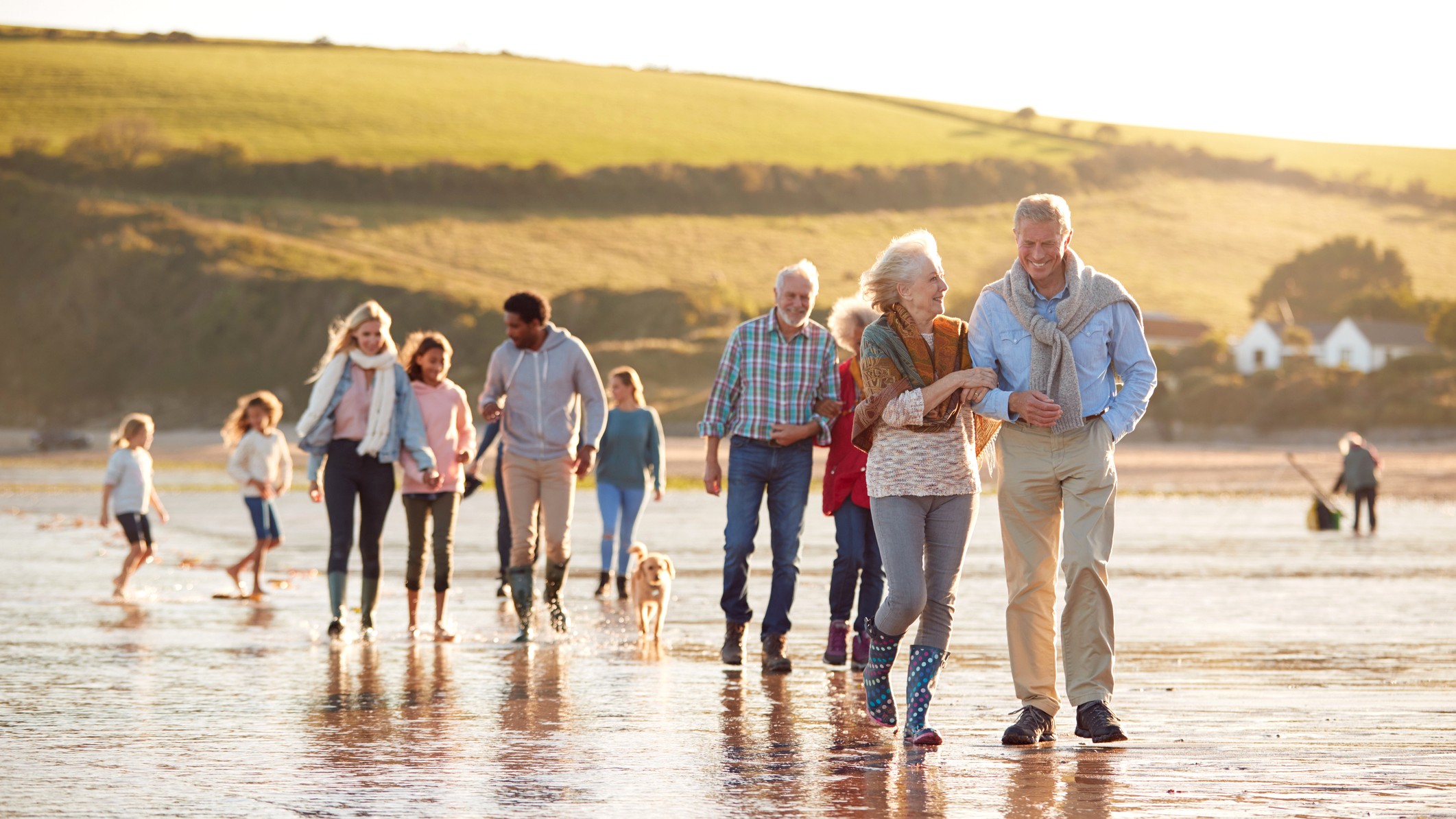 Active Multi-Generation Family With Dog Walking Along Shore On Winter Beach Vacation.