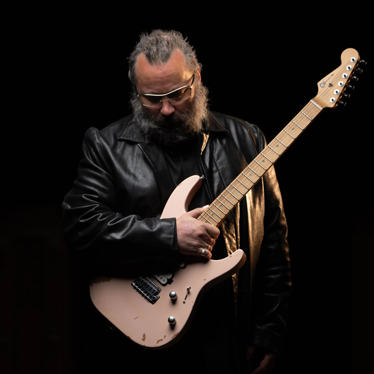 Rick Graham, dressed in black, looks down while holding his Charvel Signature Pro-Mod DK24 2PT guitar, finished in Shell Pink