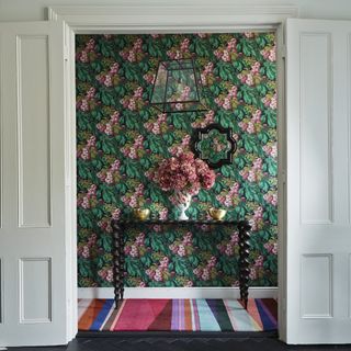 a botanical and floral theme walled paper with green leaves and pink flowers in a hallway with entrance table
