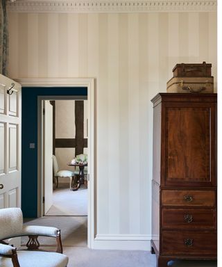 Cream subtle vertically striped wallpaper on a bedroom with ornate crown molding and renaissance furniture