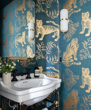 A bathroom with blue wallpaper with gold cheetahs, a mirror, and a white sink