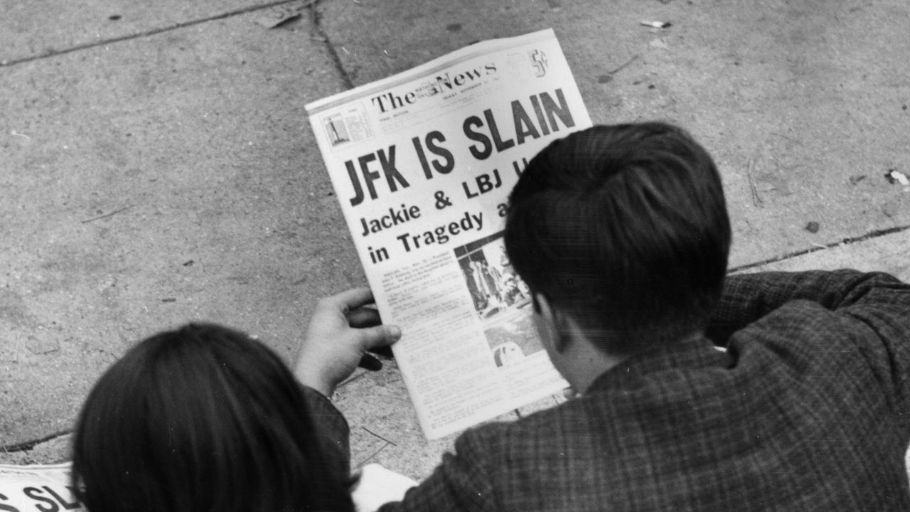 25th November 1963: Two people in Lafayette Park, Washington, reading the newspaper reports of President John F Kennedy&#039;s assassination.