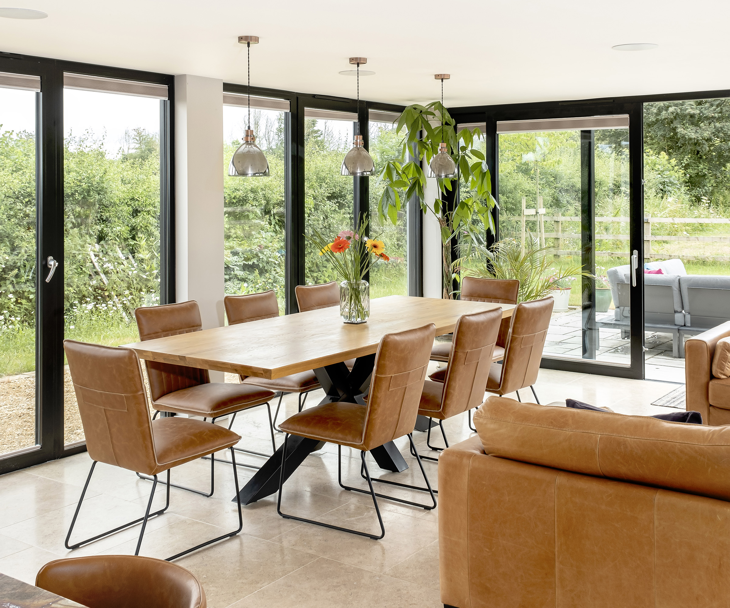 A large dining table with tan leather dining chairs with glass sliding doors and windows